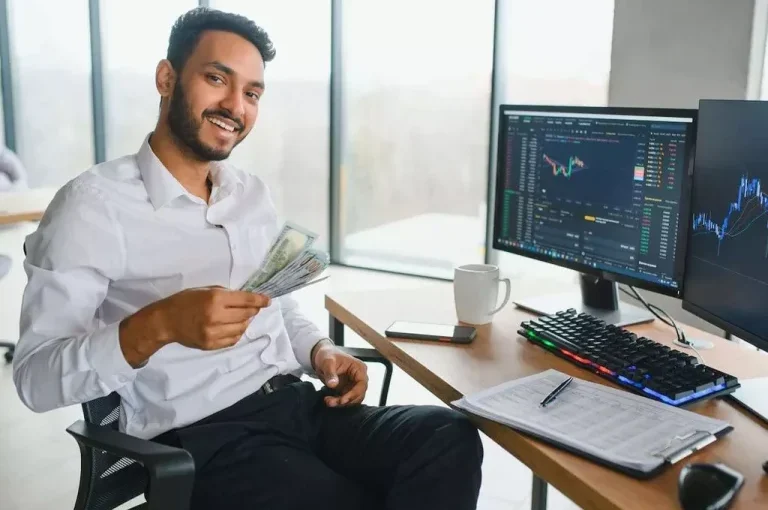 Smiling man holding cash at trading workstation