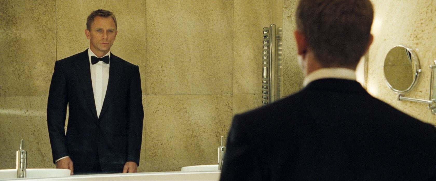 Man in tuxedo looking into bathroom mirror